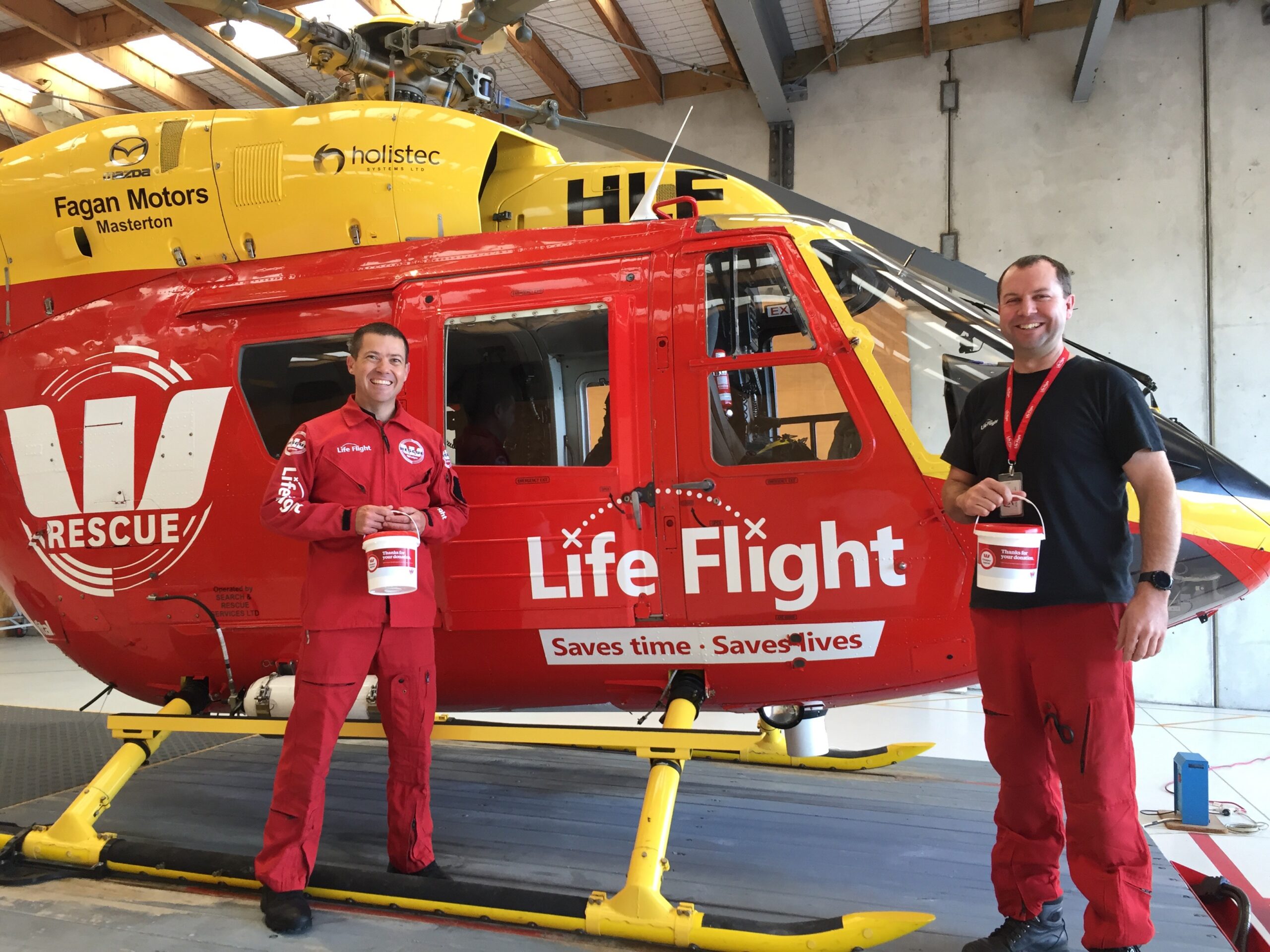 Two men in uniform in front of Westpac Chopper holding collection buckets