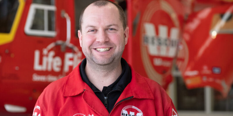 Male in flight suit smiling infront of Westpac Rescue Helicopter