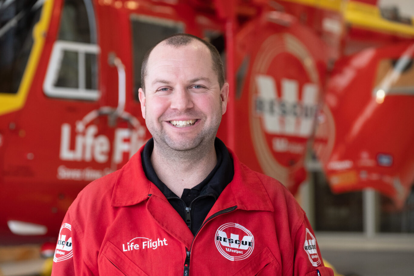 Male in flight suit smiling infront of Westpac Rescue Helicopter