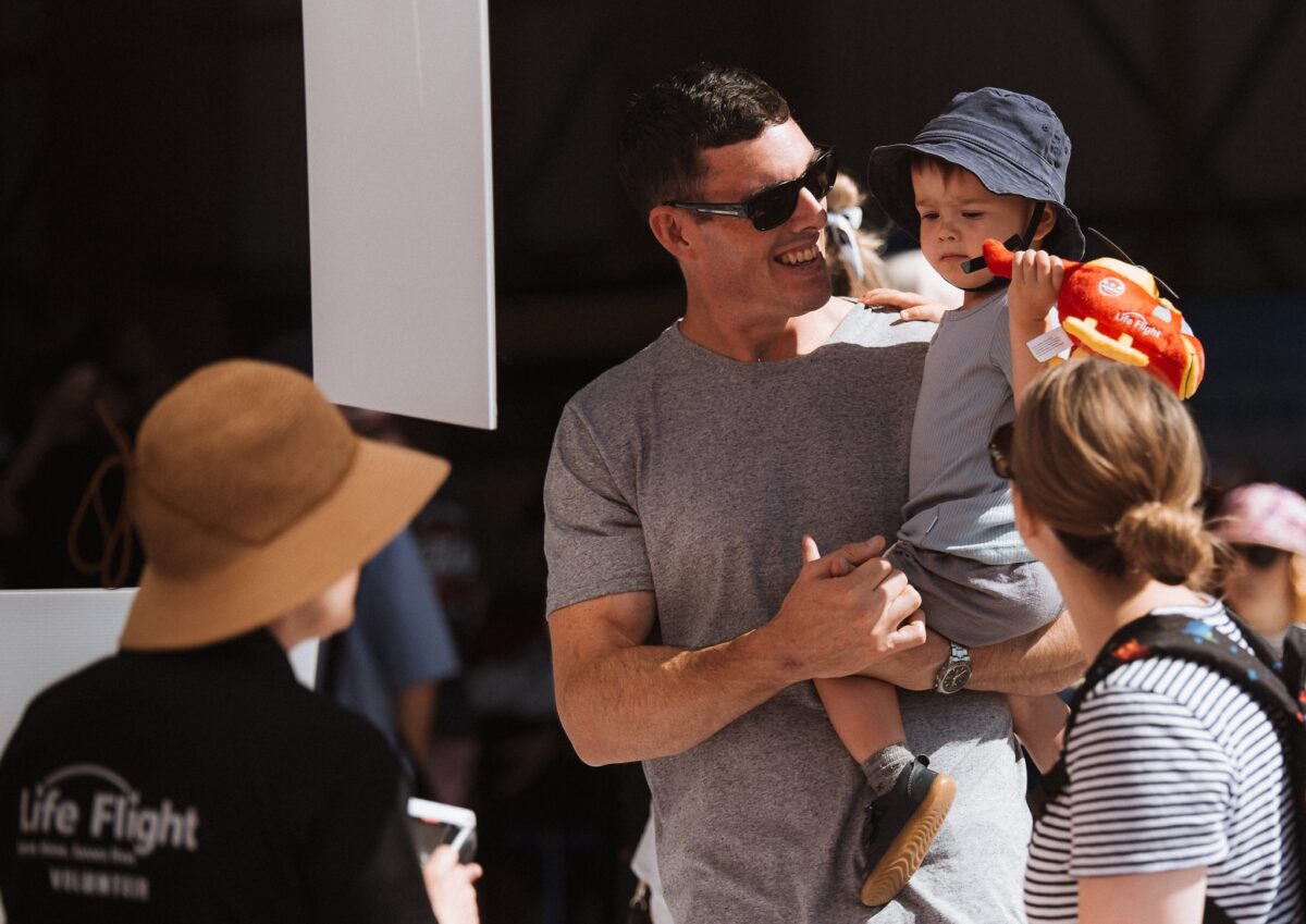 Man smiling holding a small child, volunteer in the foreground